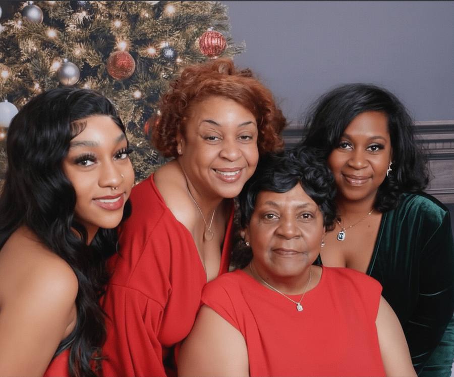 Four generations of the family together in red, in front of the Christmas tree.