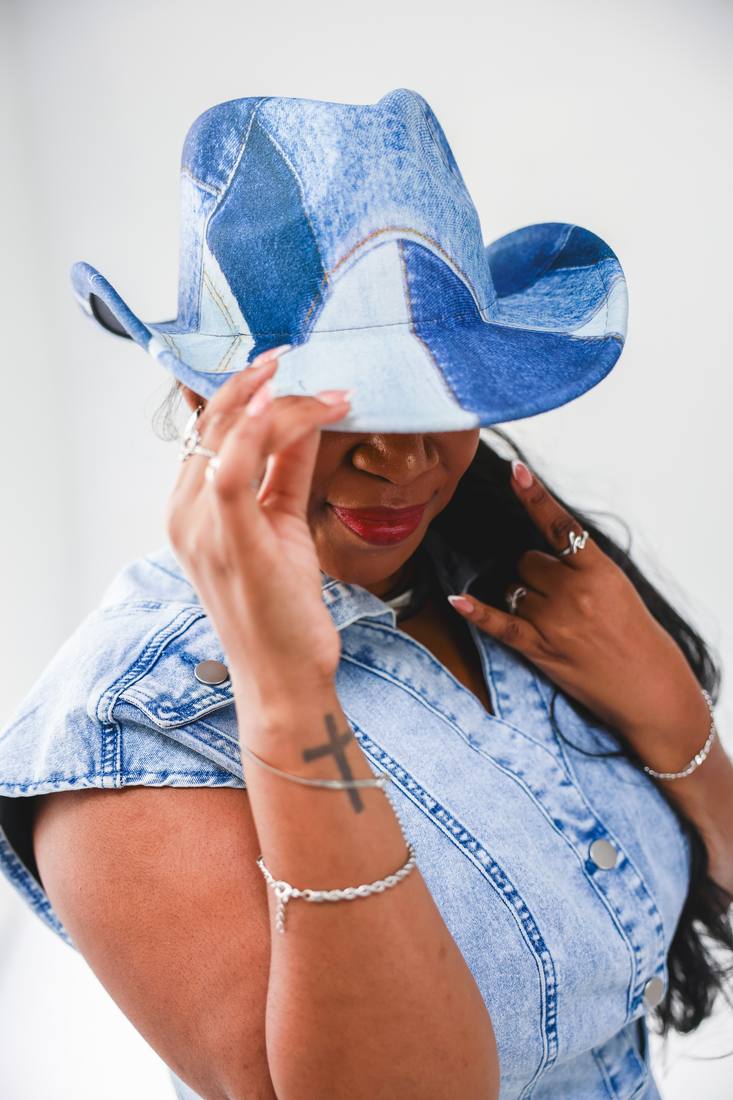 Raven laughing under the brim of a denim cowboy hat.