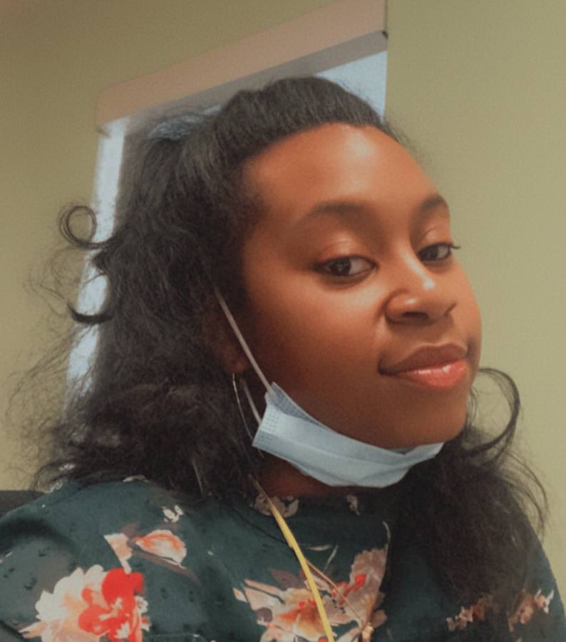 Raven at work, smiling, mask tucked under her chin.