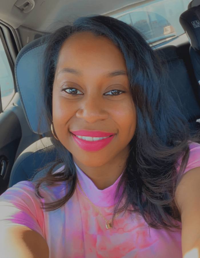 Raven smiling wide in the car, wearing a pink top.