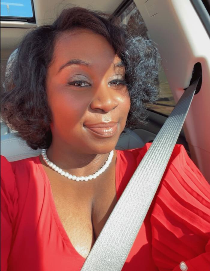 Raven in a red top and pearl necklace, smiling in golden sunlight.