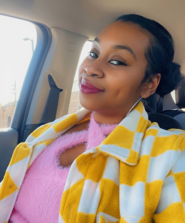 Raven in a yellow-and-white checked jacket, smiling in the car.